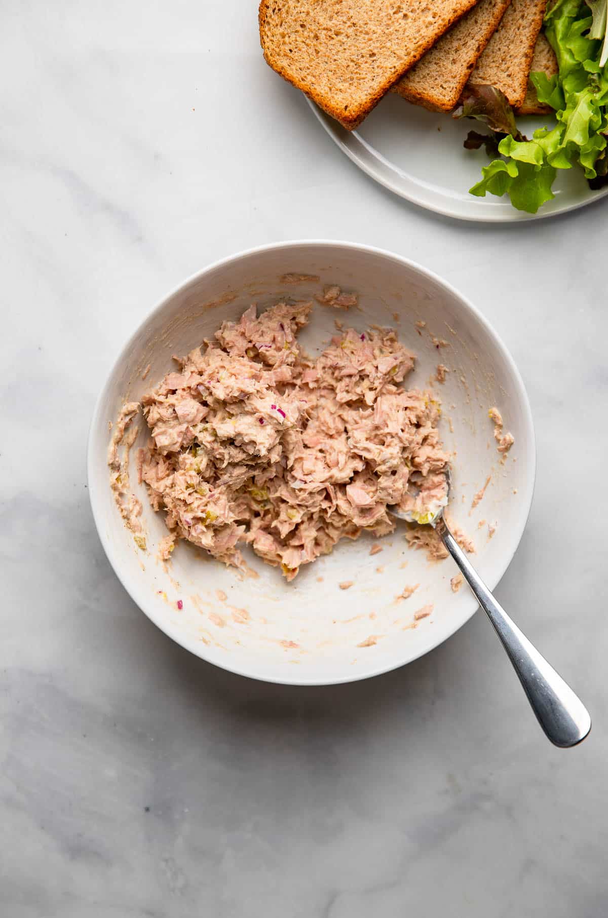 healthy tuna salad mixed together in a white bowl with a fork.